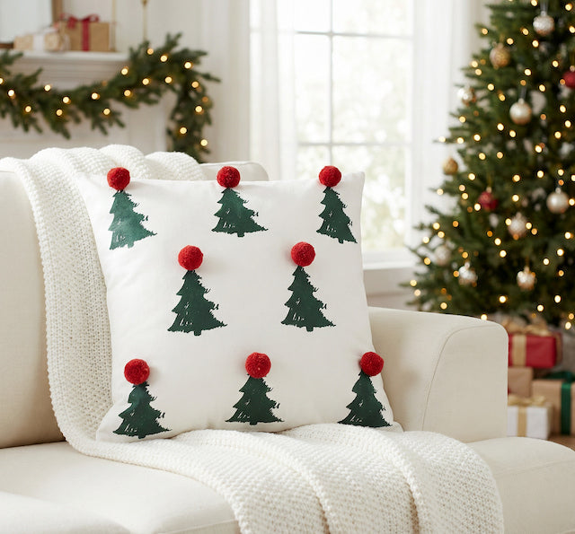 Cream Christmas cushion cover with green tree design and red pom pom details on a festive sofa