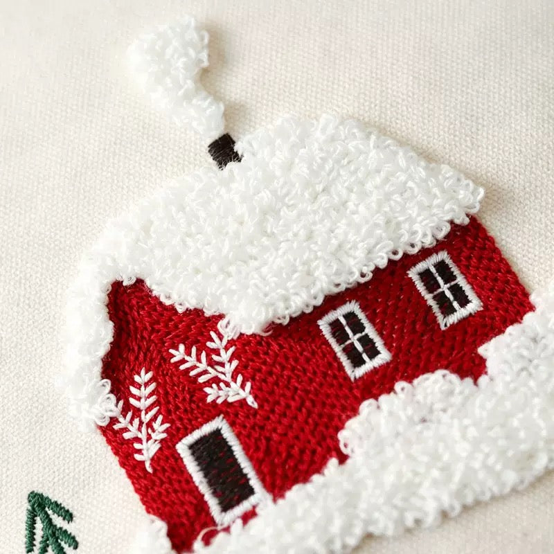 Close-up of a red house-shaped embroidered design with a white snowy roof and trim, on a light beige fabric background.