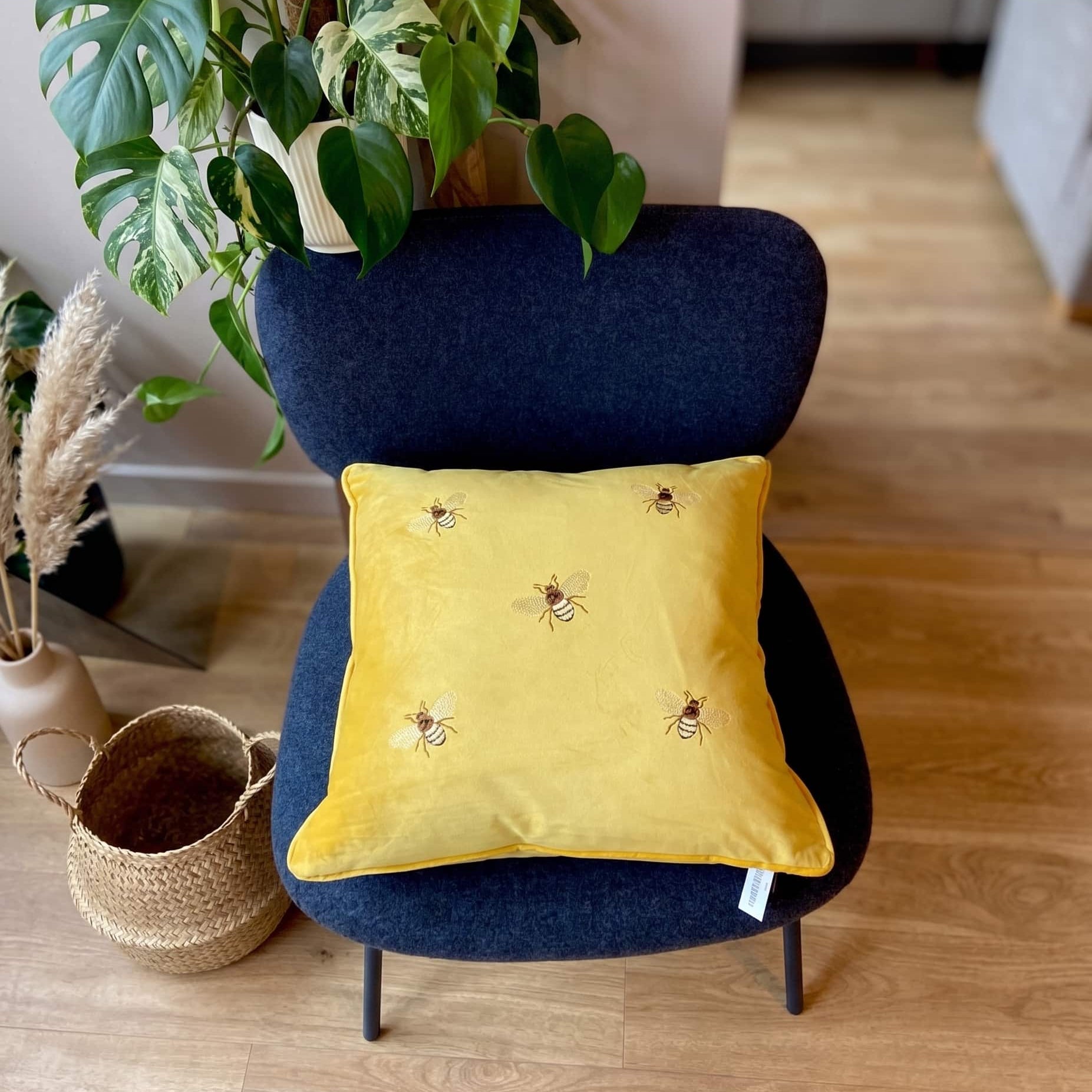 Yellow pillow with bee patterns on a blue chair in a room with plants and decor.