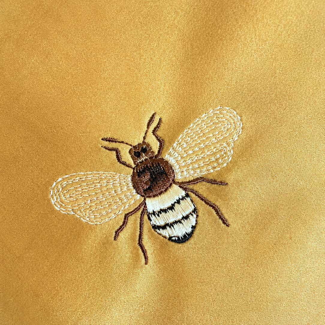 Close-up detail of handcrafted bee embroidery on velvet cushion