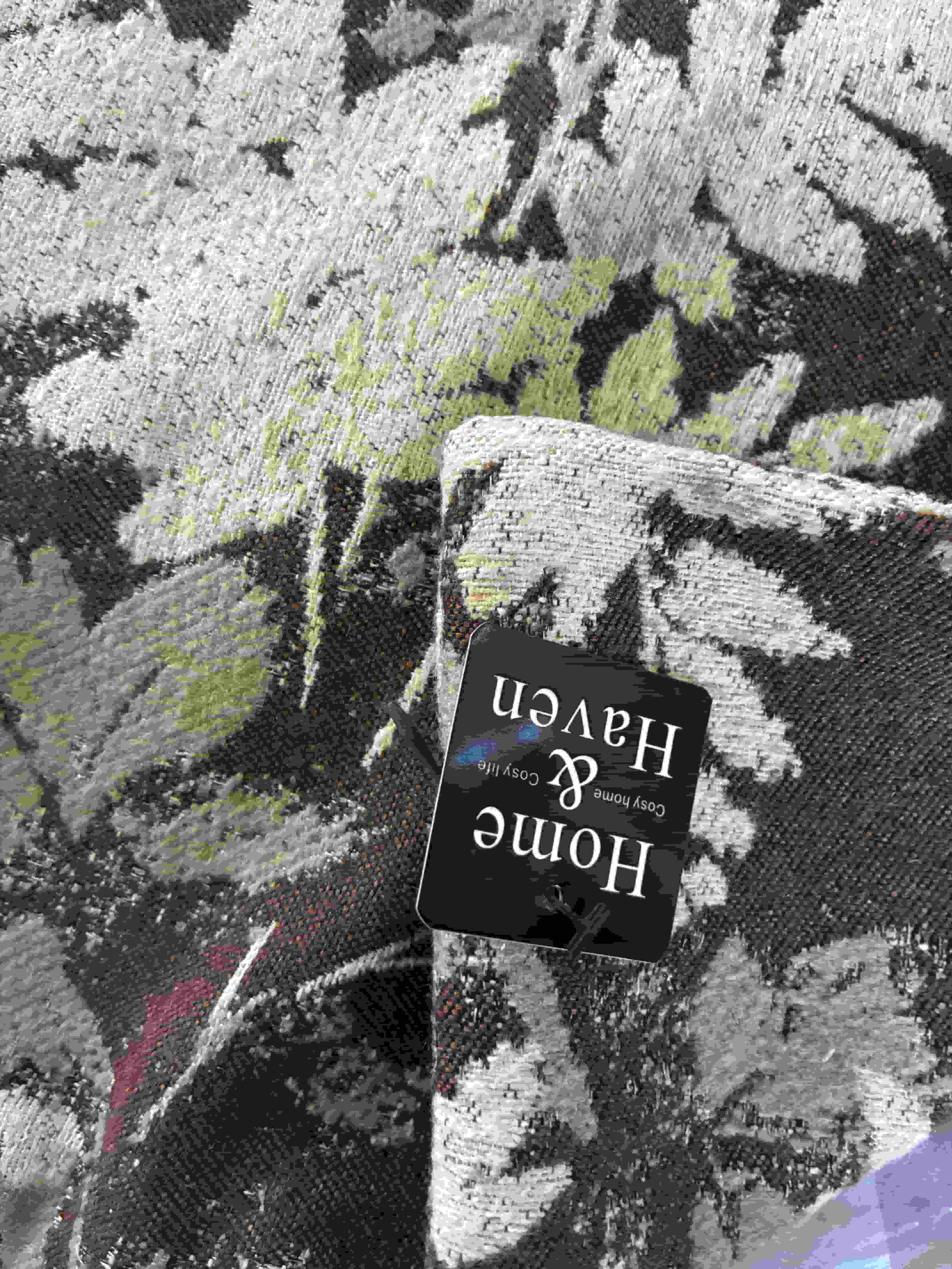 Close-up of the woven botanical texture showing the black Home & Haven brand label stitched onto the side of a cushion cover.