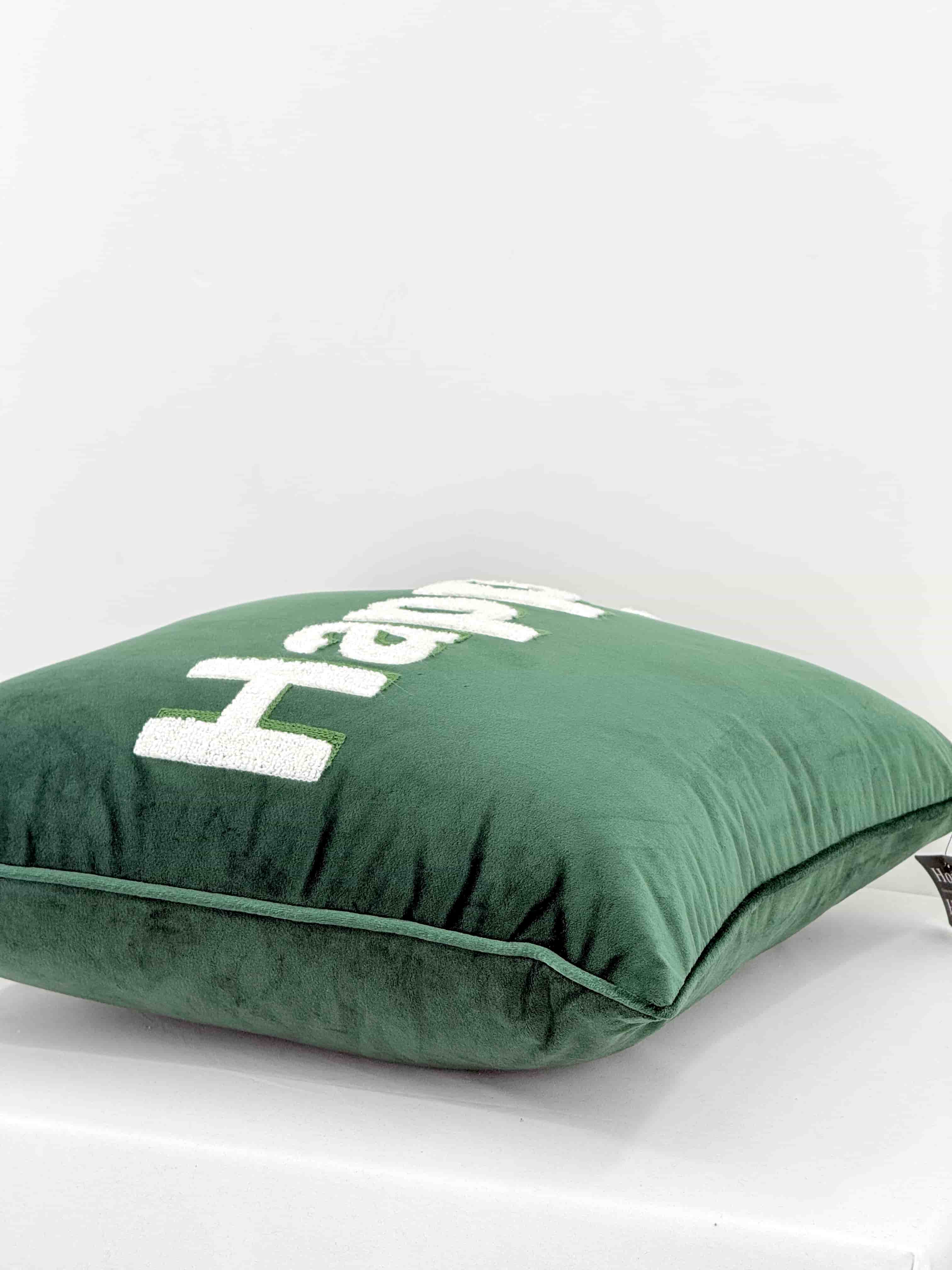 Side angle view showing the thickness, piped edge, and soft velvet texture of an emerald green Happy embroidered throw pillow.