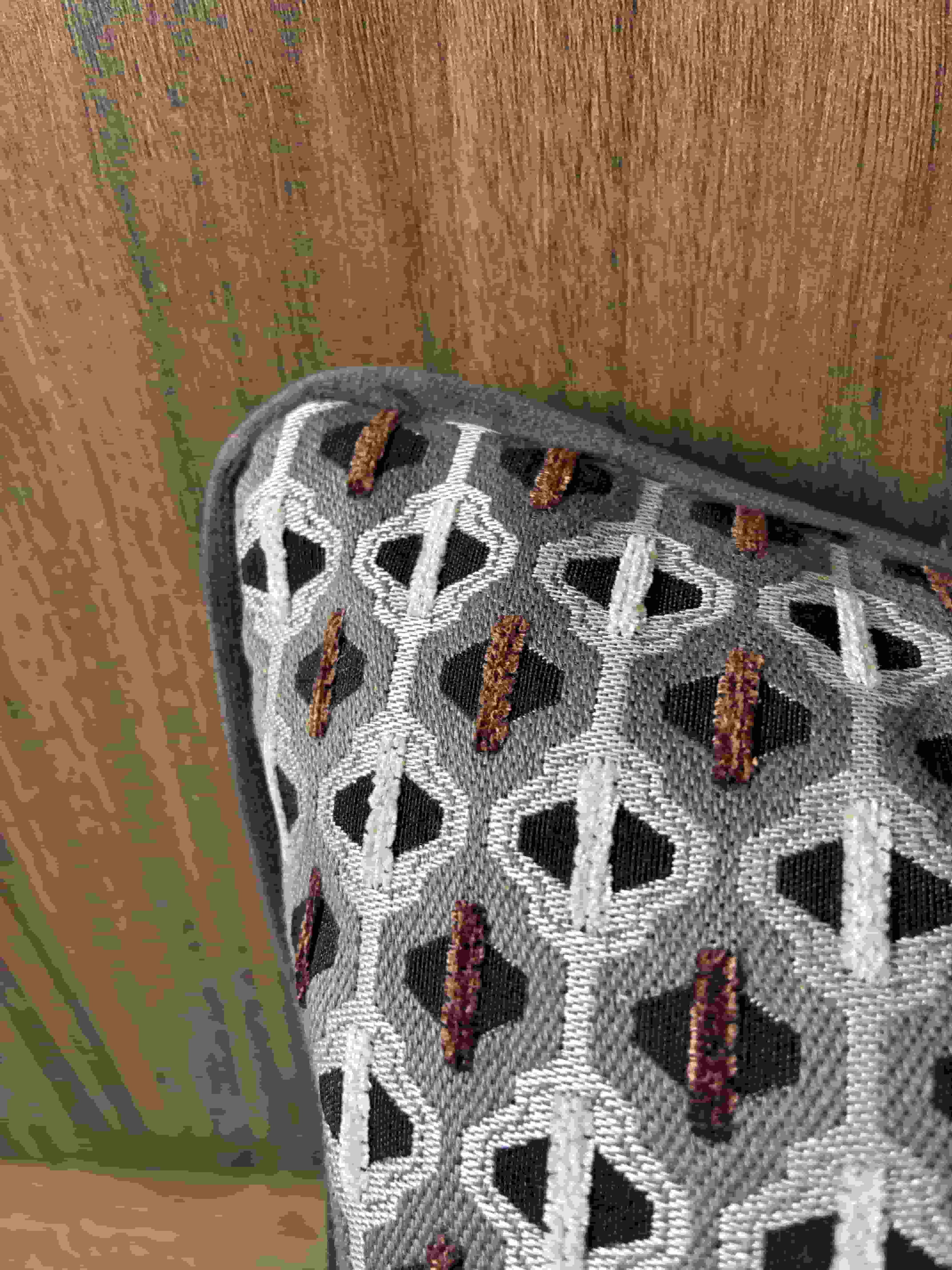 Close-up of a textured grey geometric woven cushion cover featuring white interlaced patterns, black diamond spaces, and small dark red-brown embroidered stitch accents.