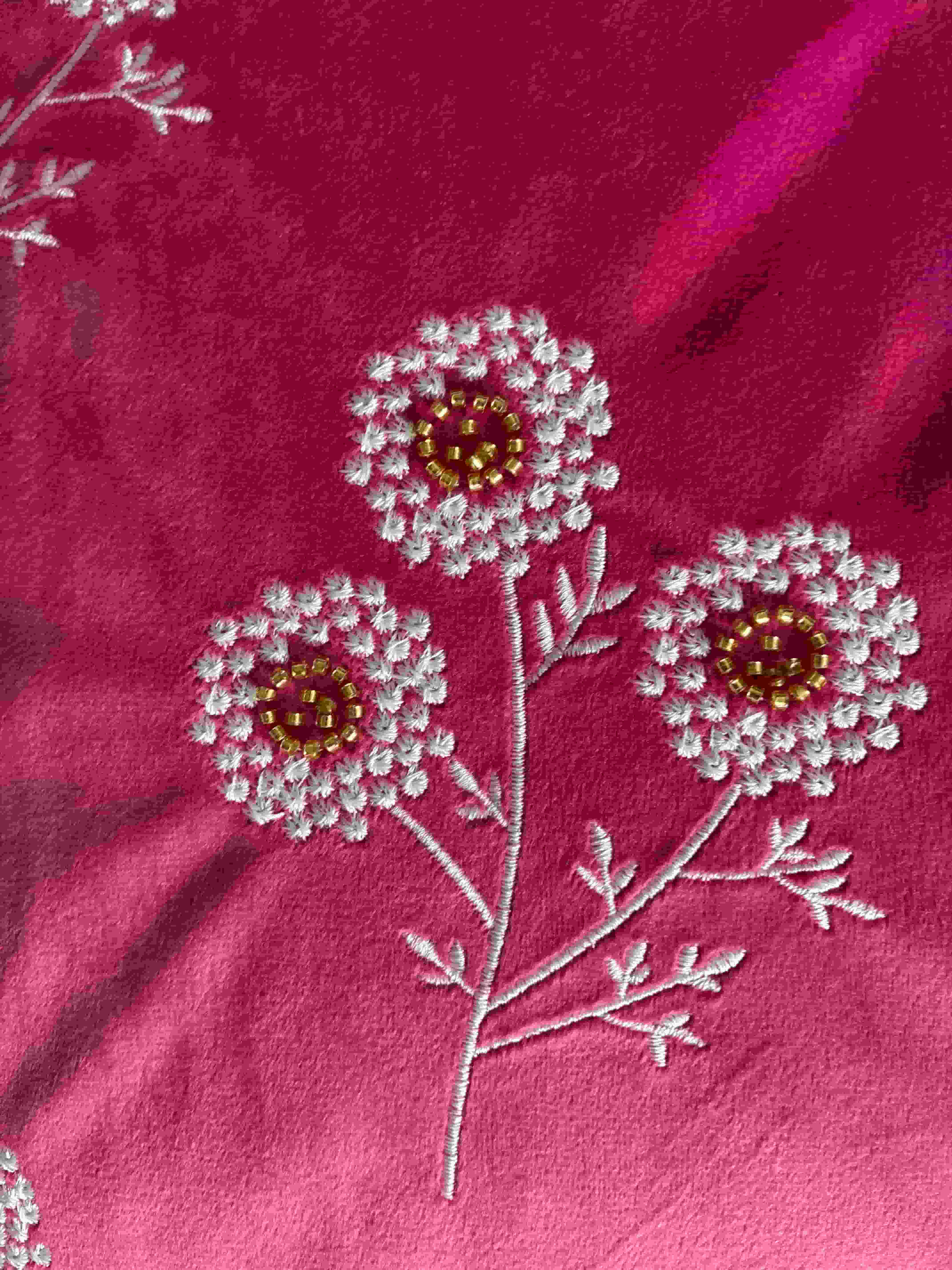 Close-up detail of white embroidered wildflowers with delicate gold tube bead centers stitched onto a vibrant pink velvet cushion cover.