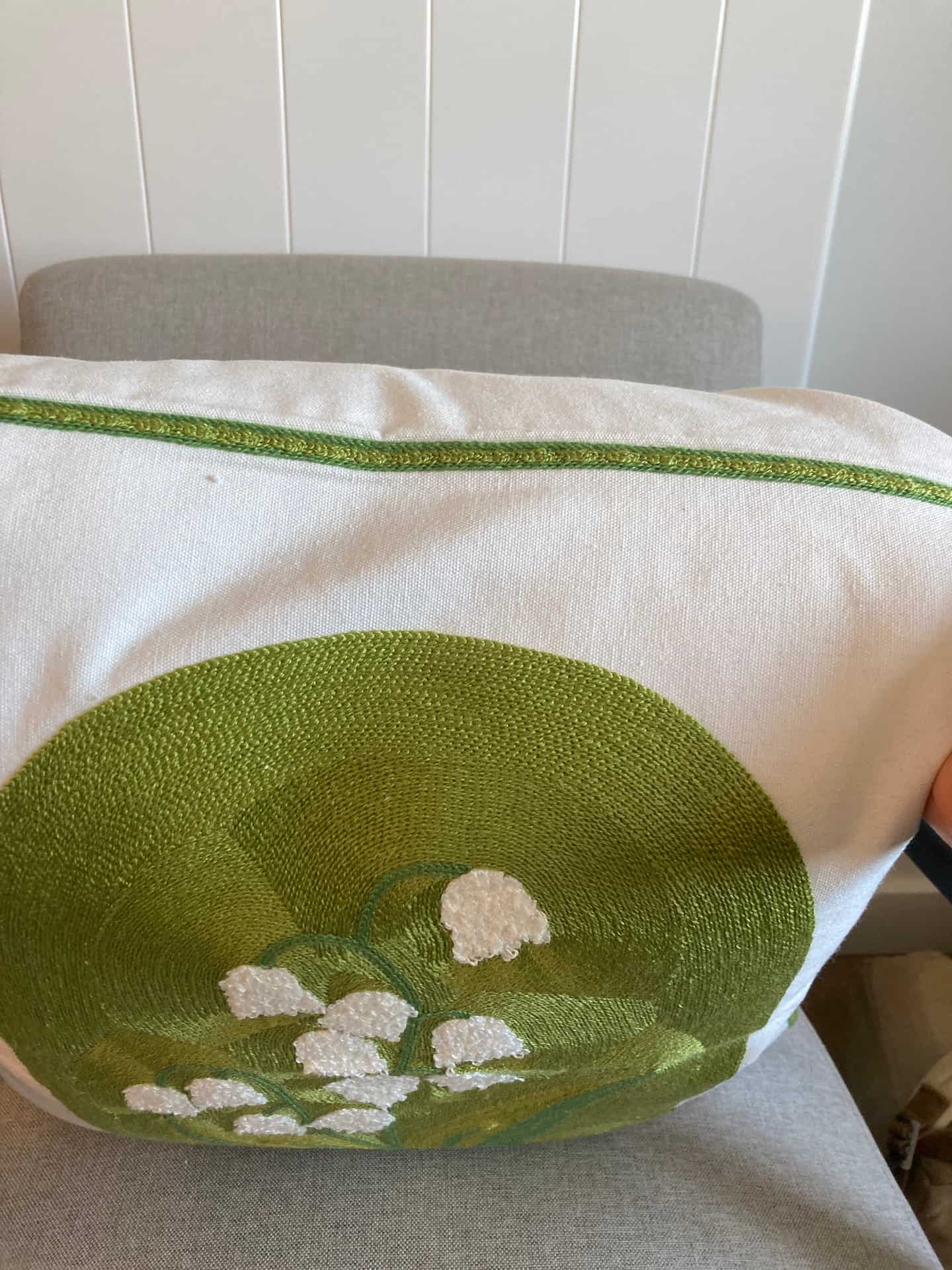 Side view of a cream cushion cover featuring a textured green stitched pattern, white bell flowers, and a contrasting green piped edge.