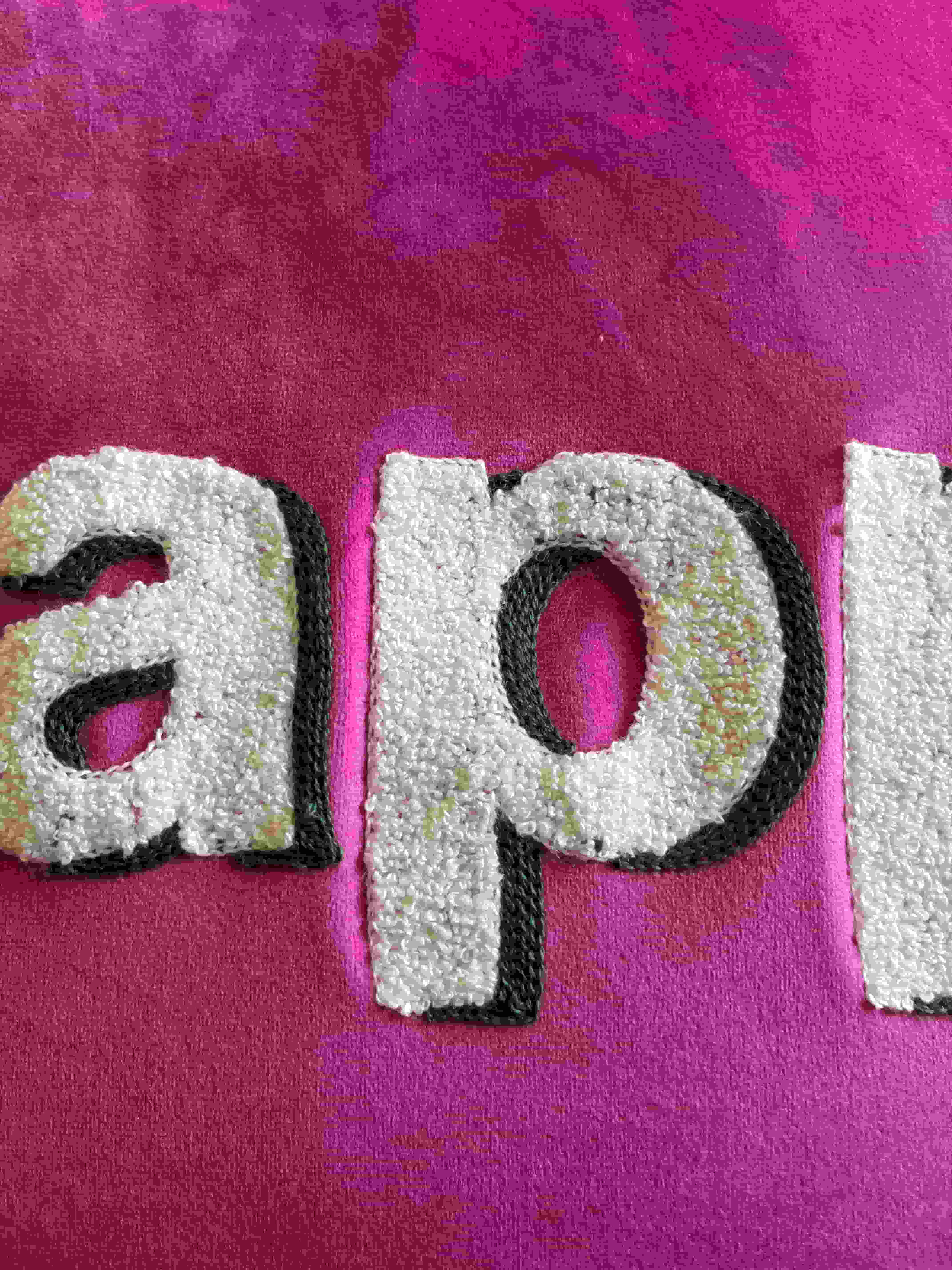 Close-up of white textured "Happy" embroidery with dark outline stitching on a bright hot pink velvet cushion cover fabric.