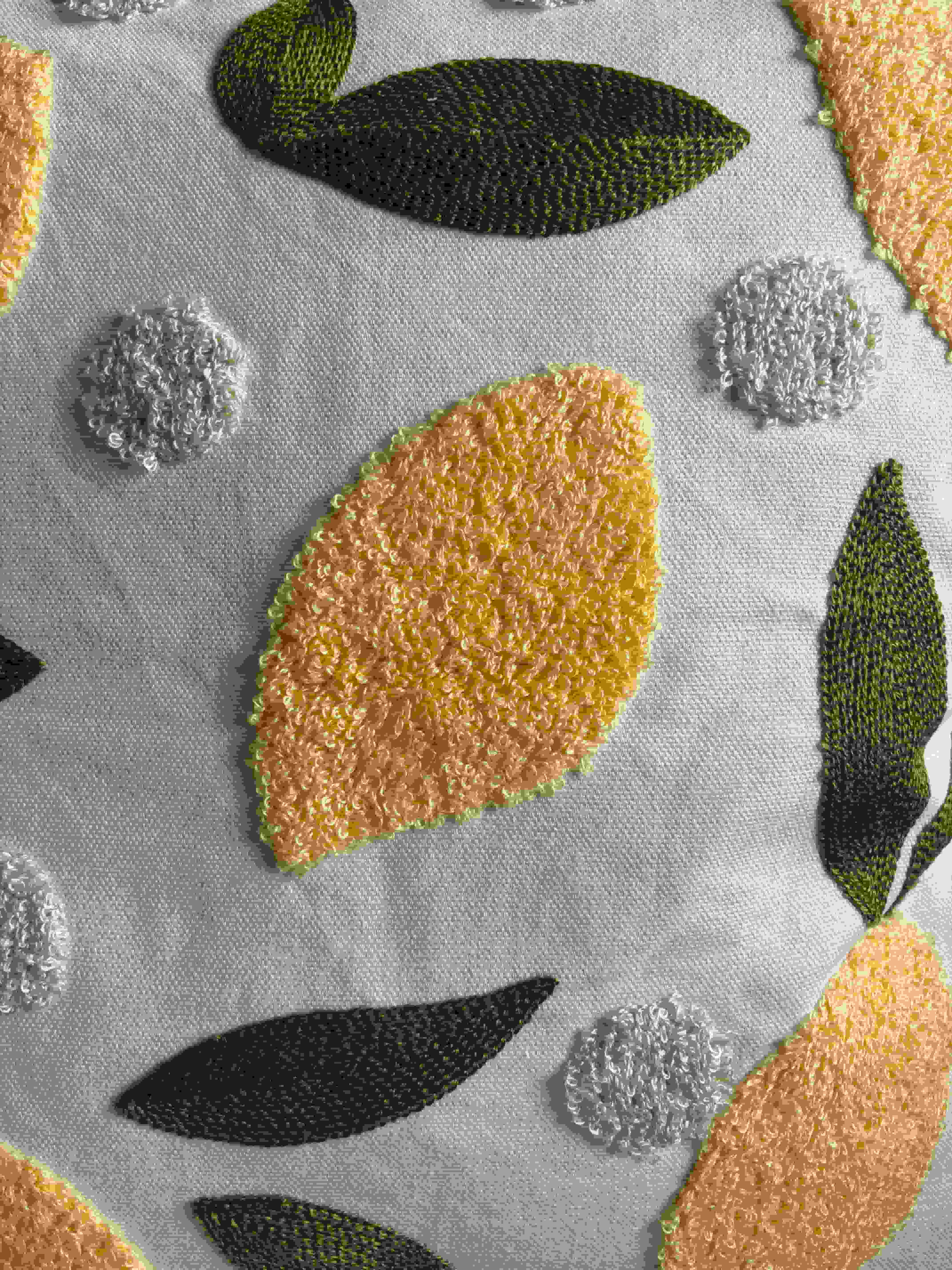 Macro shot of textured yellow citrus embroidery and green leaf stitching on a white fabric cushion cover, highlighting the artisan craftsmanship.
