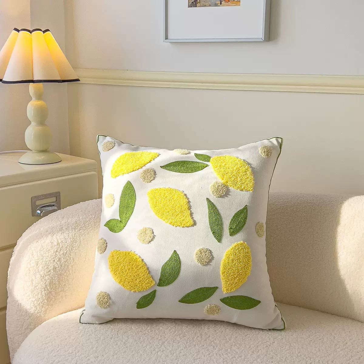 Yellow lemon embroidered cushion cover placed on a cozy white textured armchair next to a scalloped beige table lamp.
