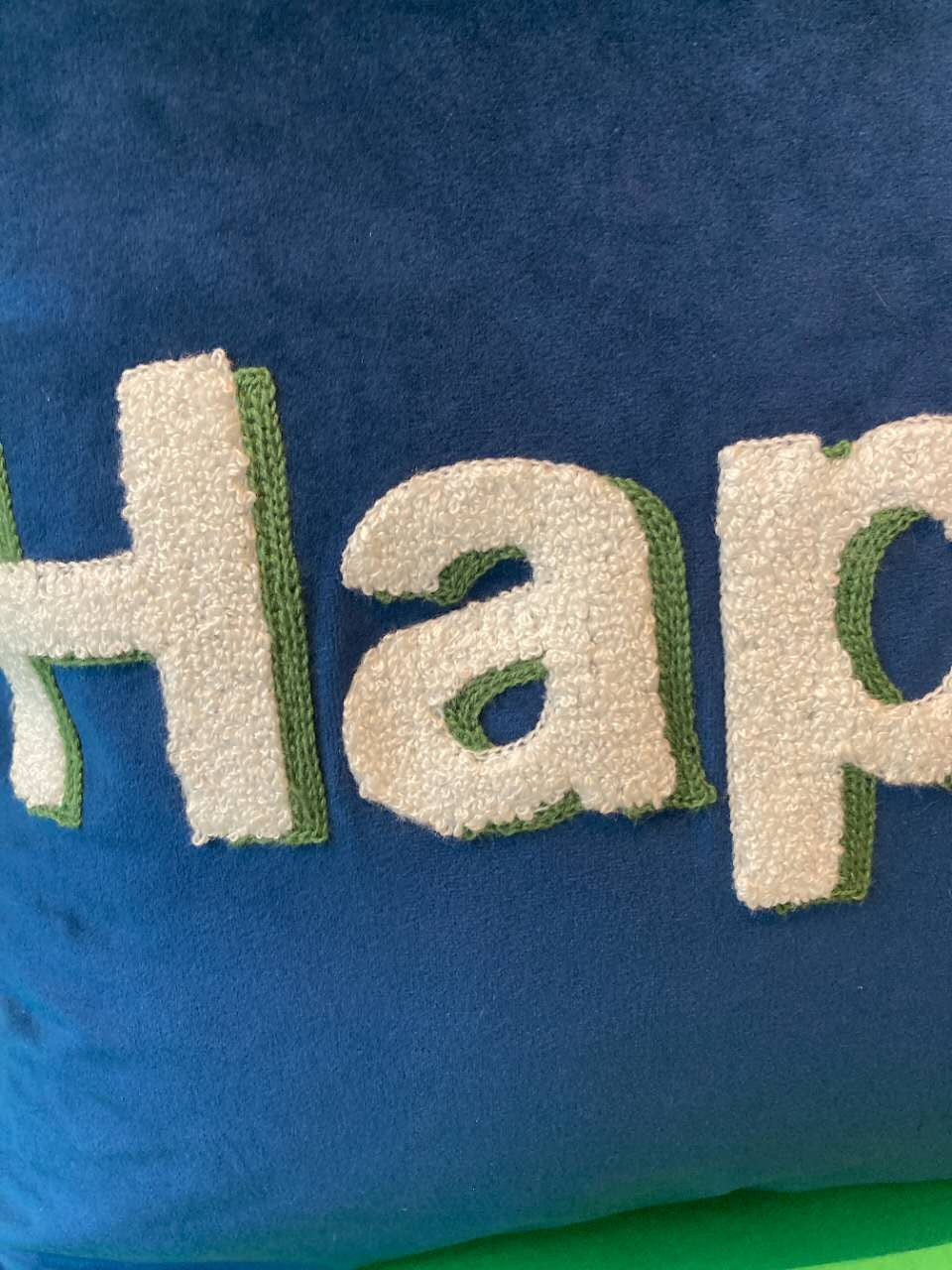 Close-up shot of white textured embroidered "Happy" lettering with green outline stitching on a navy blue velvet cushion cover.