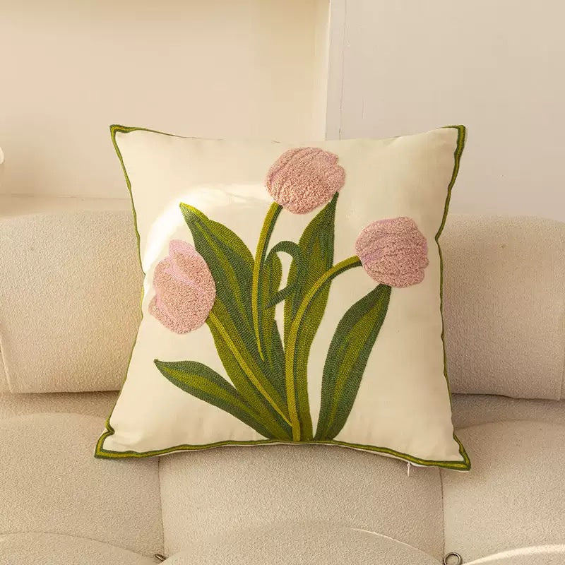 Front view of an off-white square cushion cover featuring three pink tufted tulip flowers and stitched green leaves on a neutral sofa.