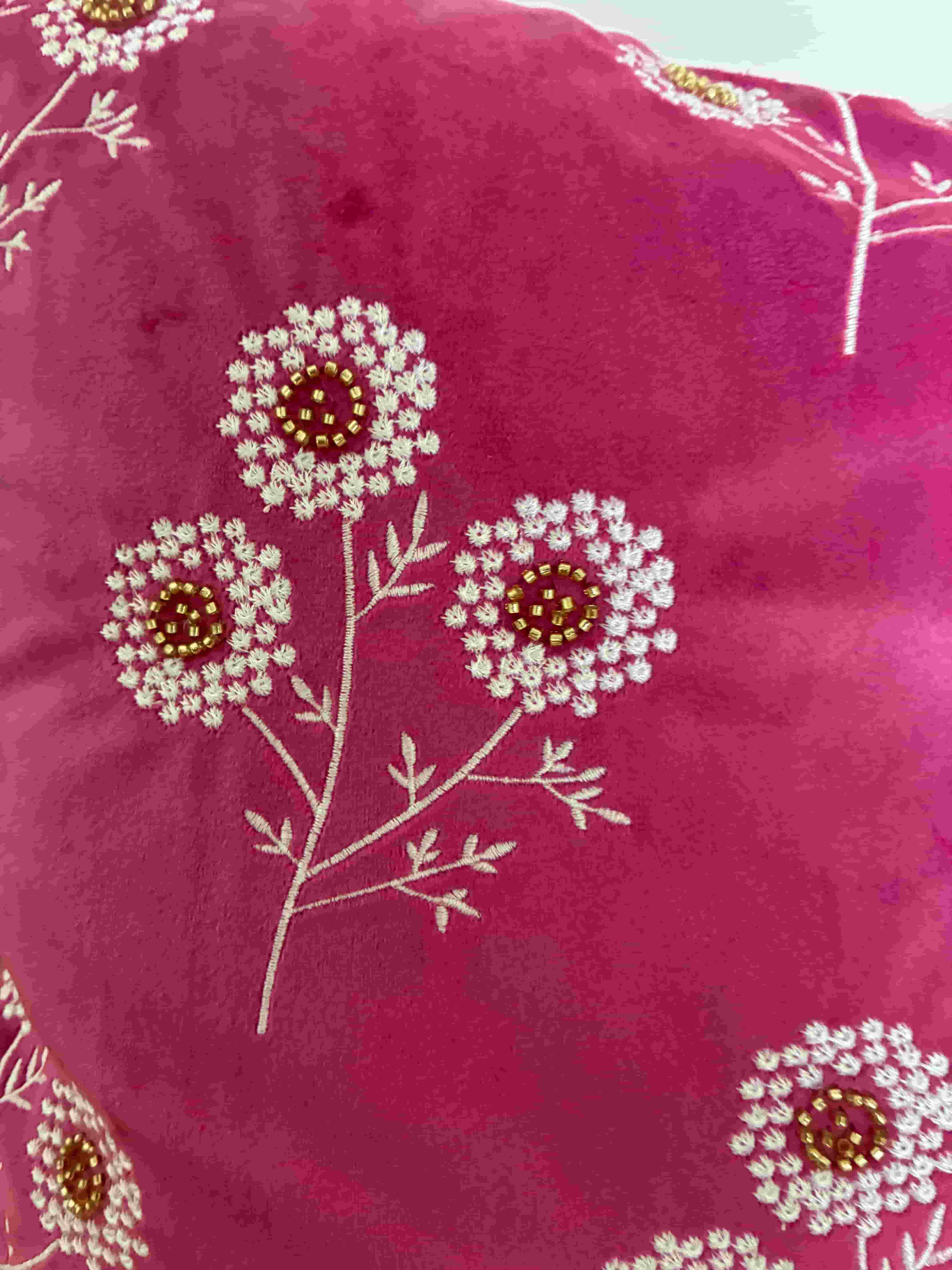 Macro shot of white embroidered floral stems and leaves with gold bead embellishments on a bright pink velvet fabric cushion cover.