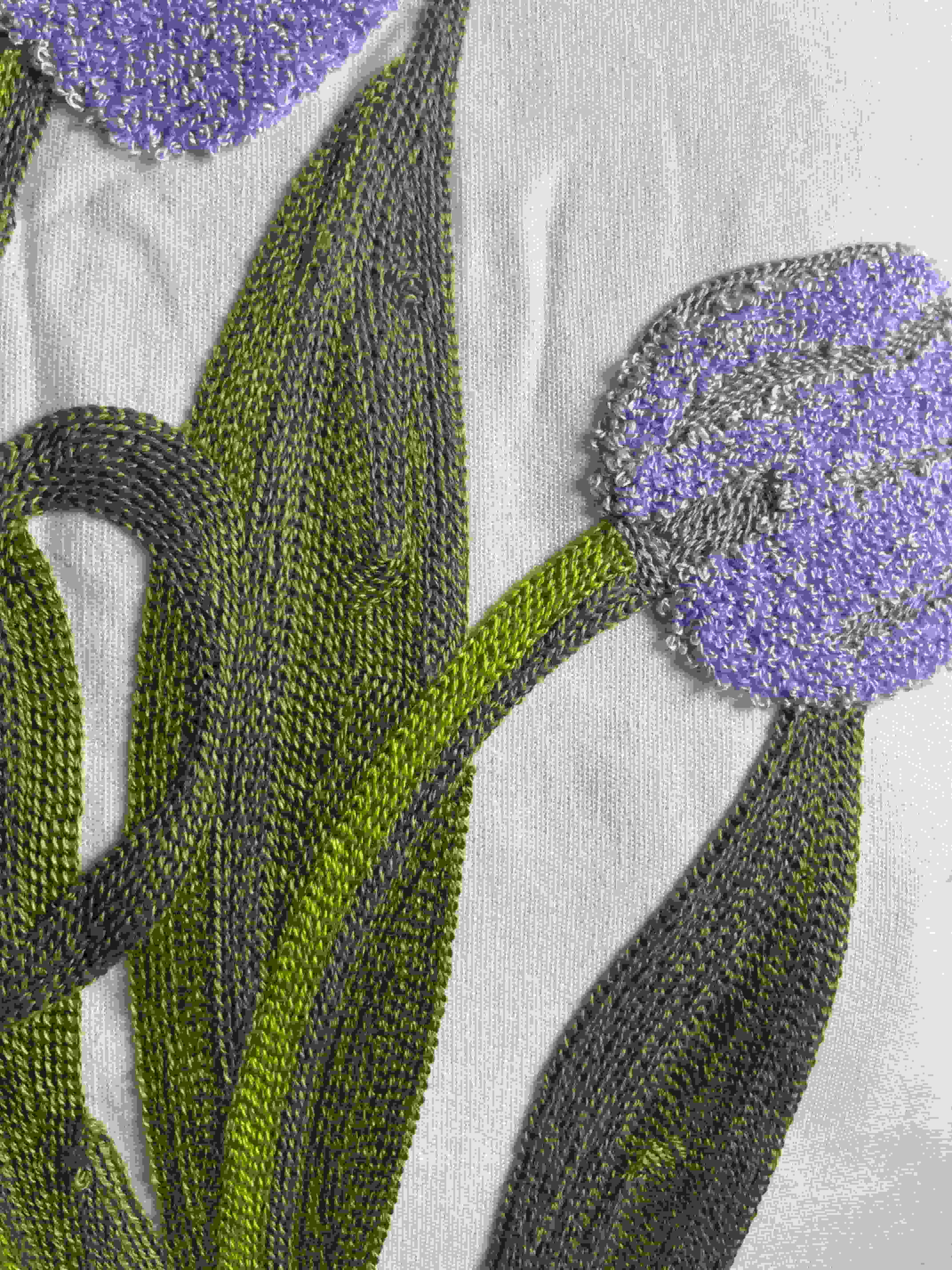 Close-up of a purple tufted tulip flower head and green stitched leaves on a cream fabric cushion cover.