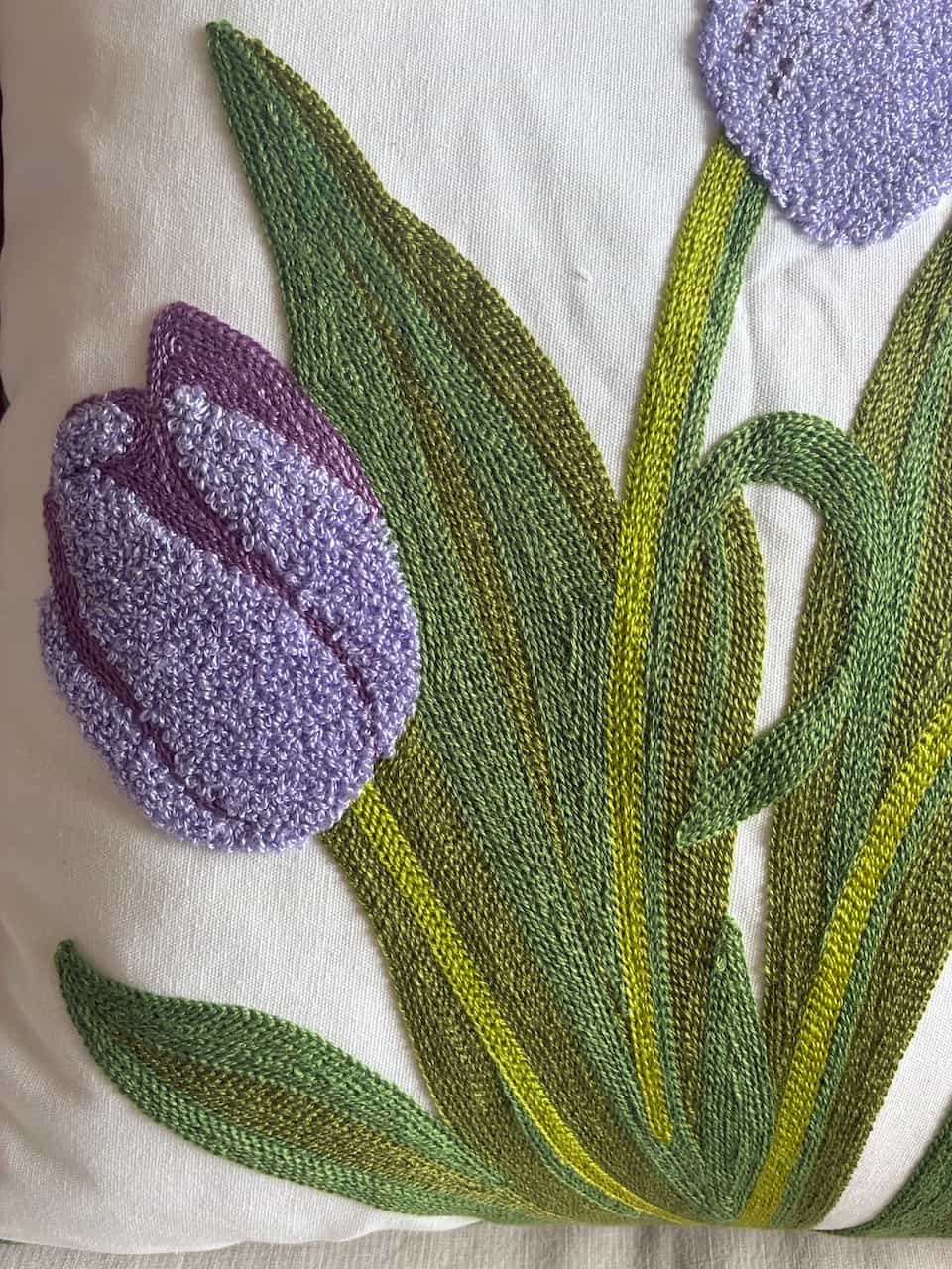 Macro shot of lavender tufted tulip petals and detailed green leaf embroidery on a white cushion cover.