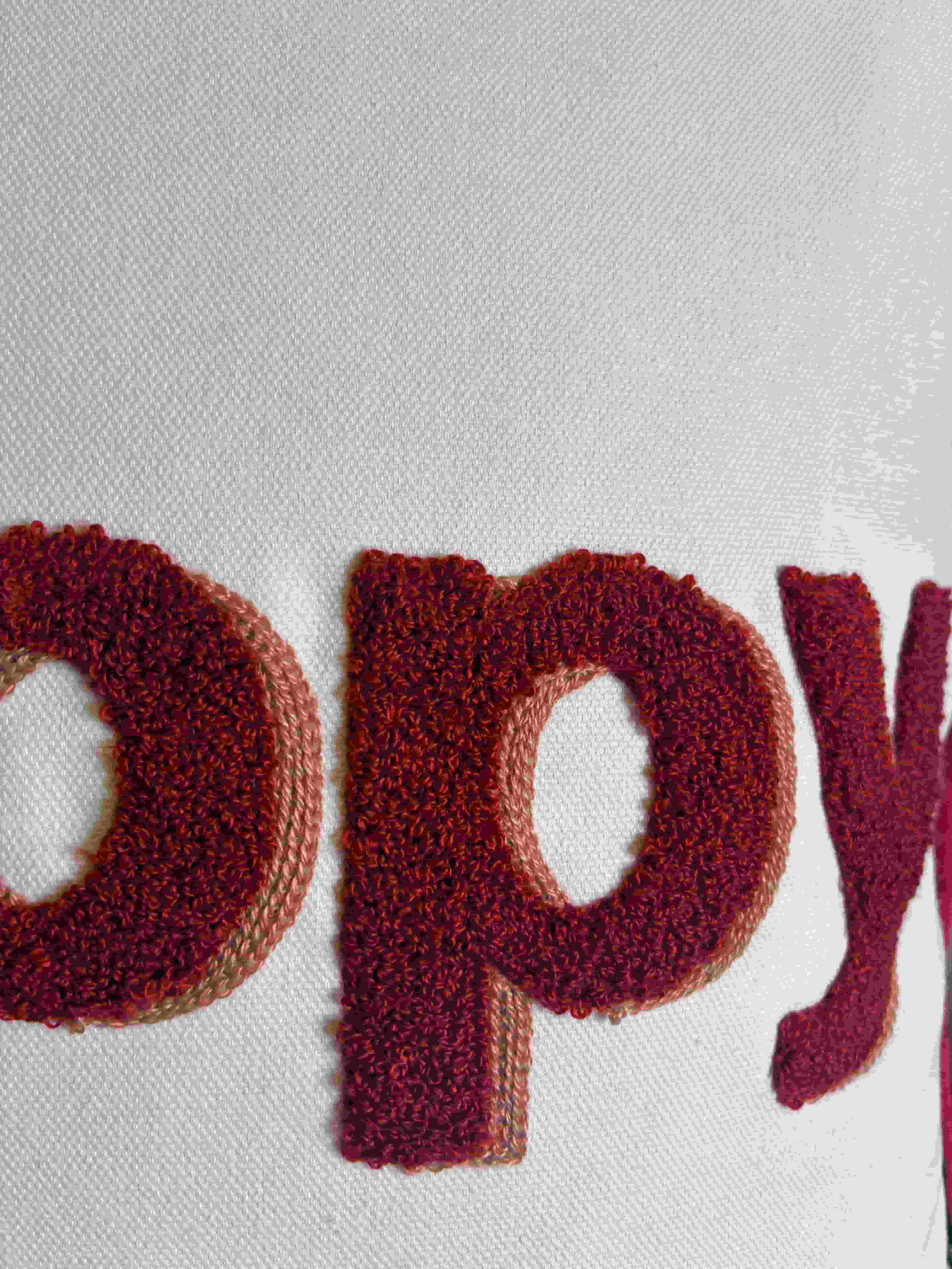 Close-up of fluffy deep red textured embroidery spelling "Happy" on a textured off-white fabric cushion cover.