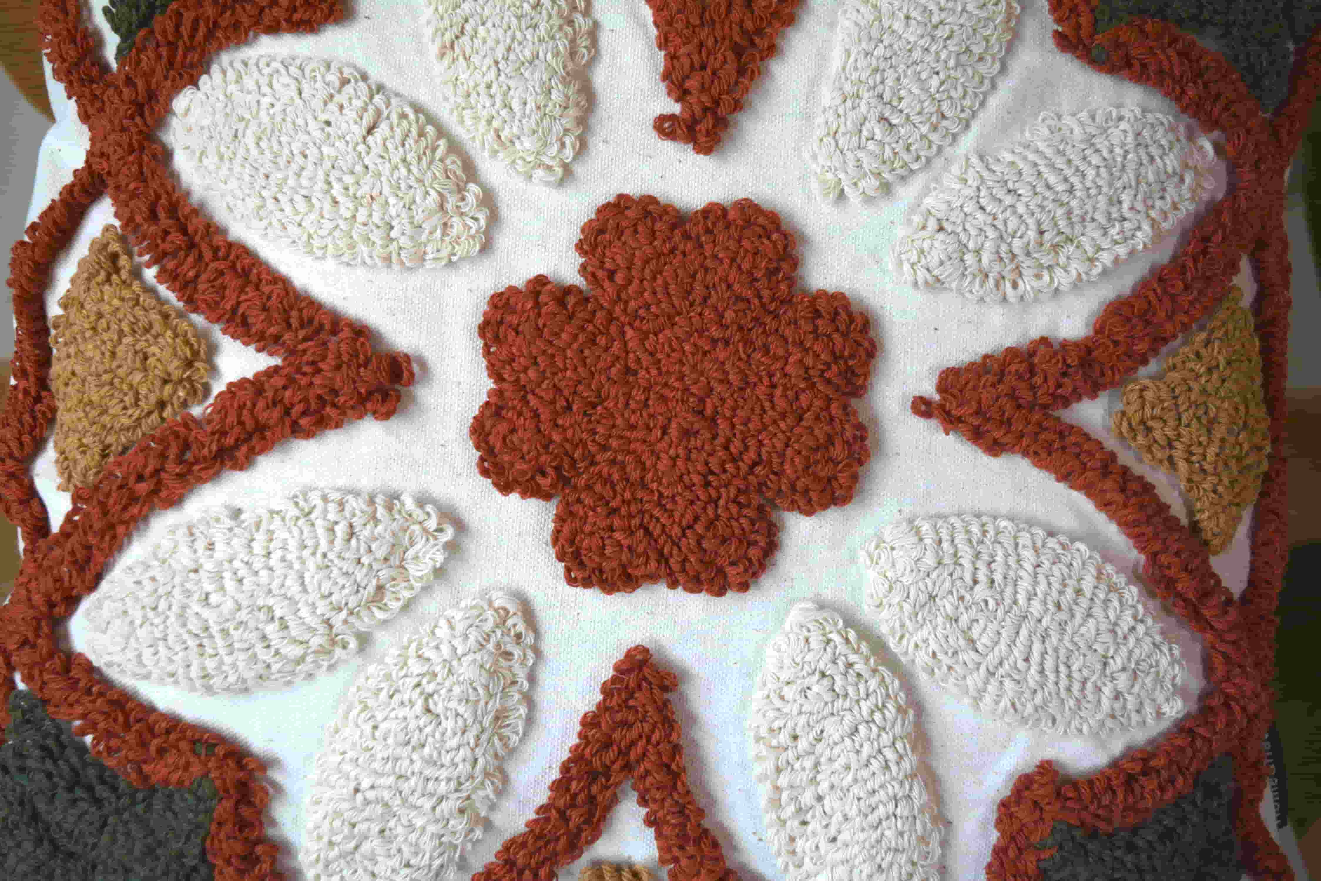 Close-up of a thick terracotta tufted central flower and cream tufted petals on a white fabric cushion cover.