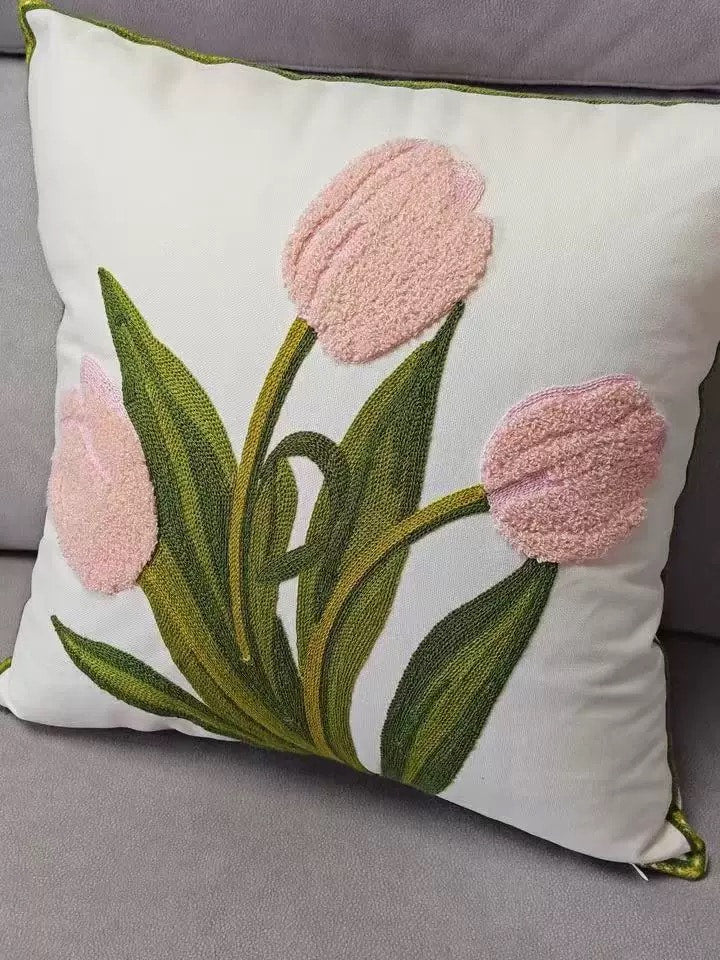 Close-up detail of pink fluffy tulip embroidery and green stem stitching on a cream fabric pillow cover with green piped edging, placed on a grey sofa.